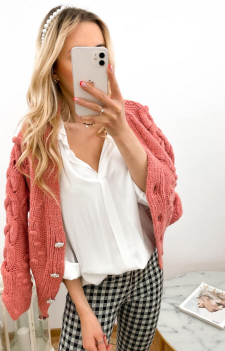 Młoda kobieta prezentuje białą elegancką koszulę i malinowy pleciony kardigan oraz eleganckie spodnie w kratkę