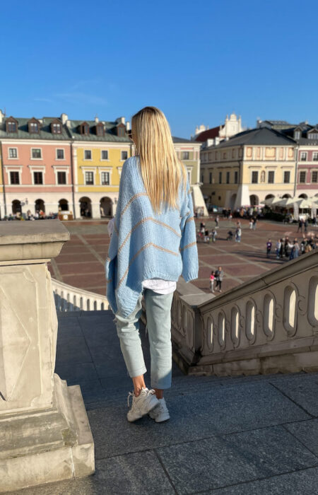 Młoda dziewczyna prezentuje błękitny pleciony kardigan i jasne jeansy