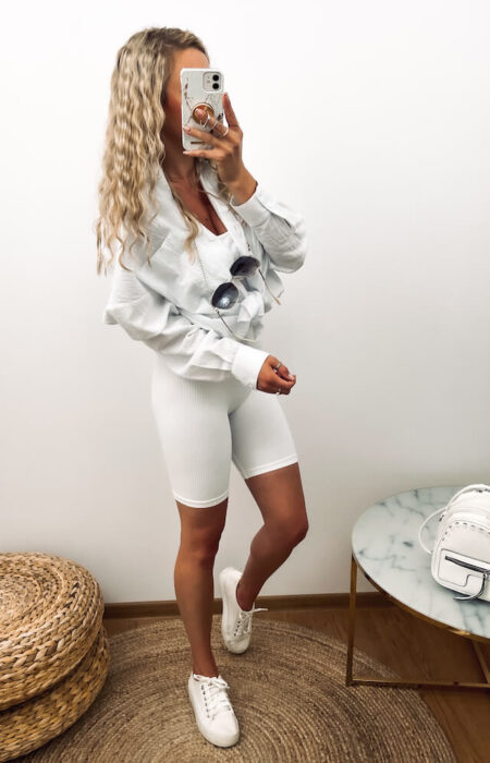 Młoda kobieta prezentuje białą elegancką koszulę w zestawieniu z białymi sportowymi kolarkami