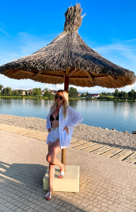 Młoda kobieta prezentuje białą elegancką koszulę z szortami i bikini