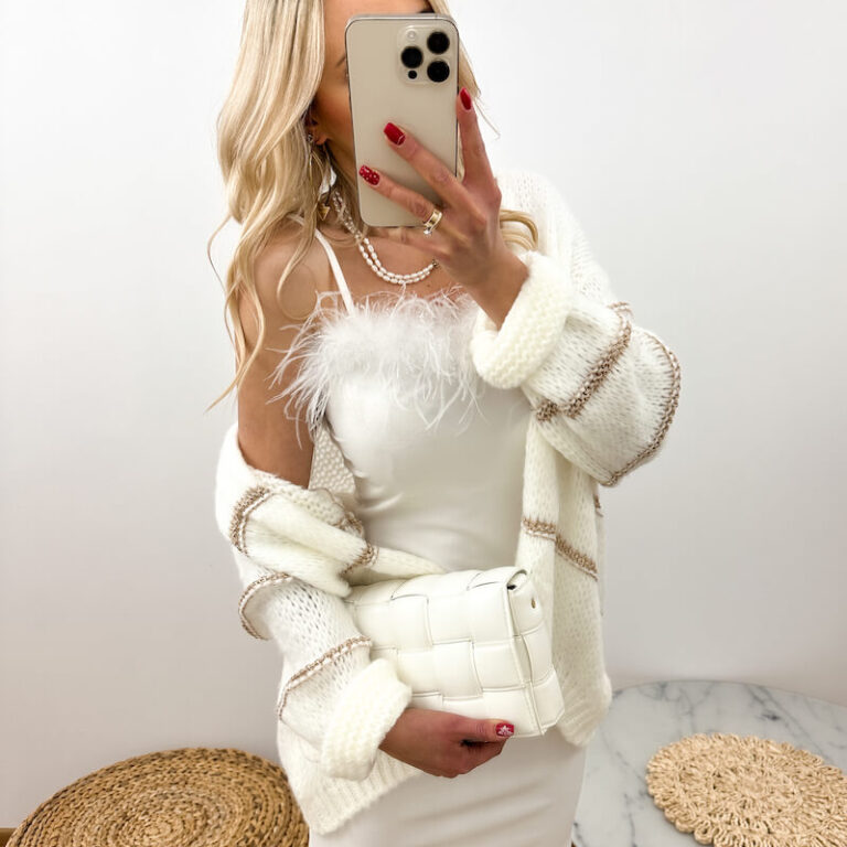 Sukienka z piórami biała o długości midi prezentowana przez młodą dziewczynę, która trzyma białą torebkę w ręku