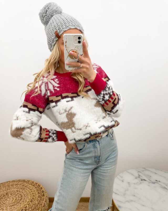 Dziewczyna prezentuje sweter w renifery i czapkę jako prezenty świąteczne