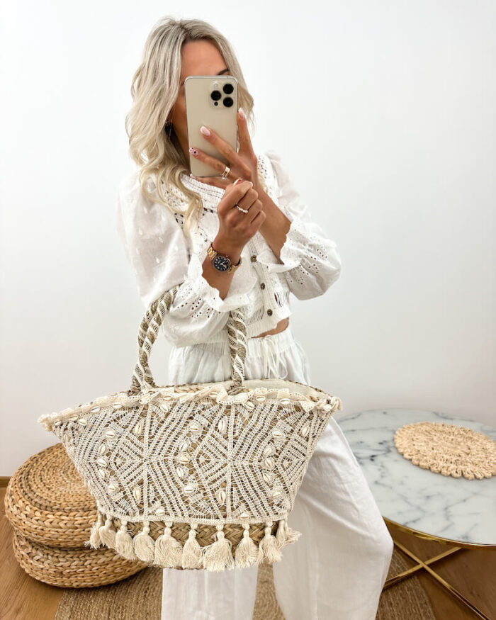 słomkowy koszyk plażowy z muszelkami i frędzlami boho prezentowany przez młodą dziewczynę w letniej stylizacji