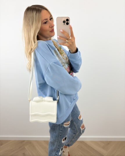 Biała torebka z kokardą mini na pasku prezentowana przez młodą dziewczynę