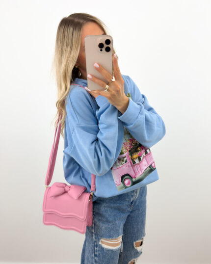 Różowa torebka z kokardą mini na pasku prezentowana przez młodą dziewczynę