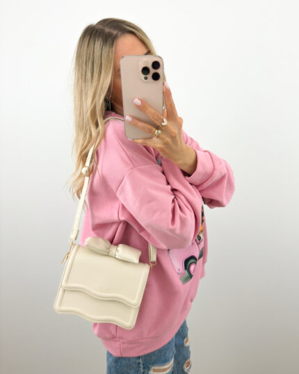Beżowa torebka z kokardą mini na pasku prezentowana przez młodą dziewczynę